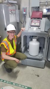Intern with safety vest and hard hat next to water tank