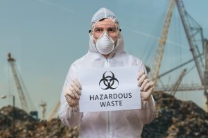 man in white haz mat suit with goggles and face mask holding hazardous waste sign
